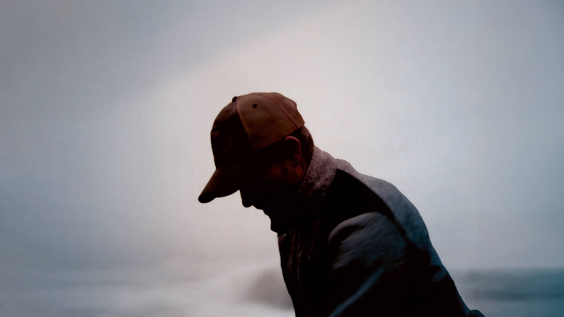 Silhuett av en svensk lantbrukare med keps som arbetar utomhus i dimmigt ljus.