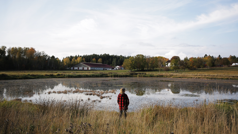 En lantbrukare står framför ett vattenfylld bevattningsdam intill åkermark.